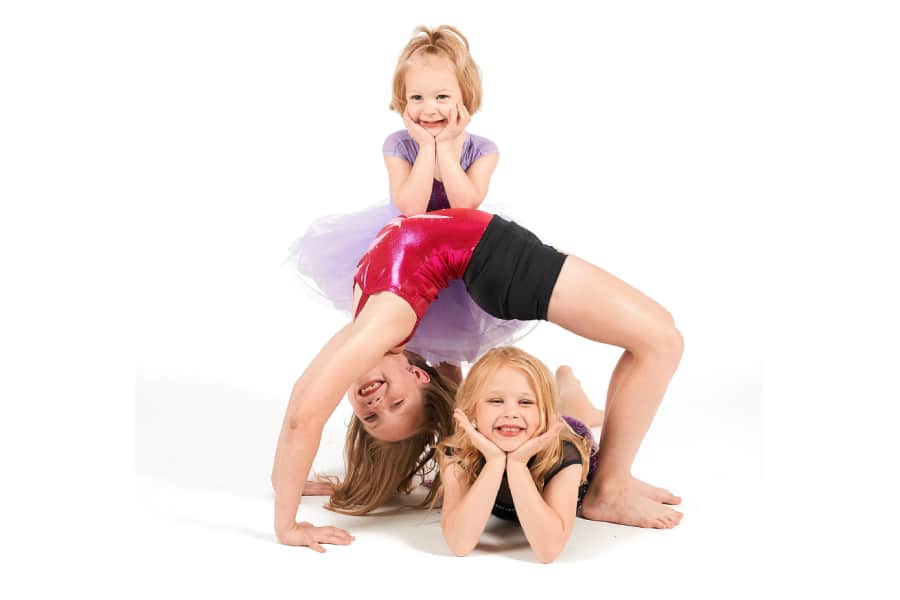 Three young girls posing for a photo with one girl doing a back flip.