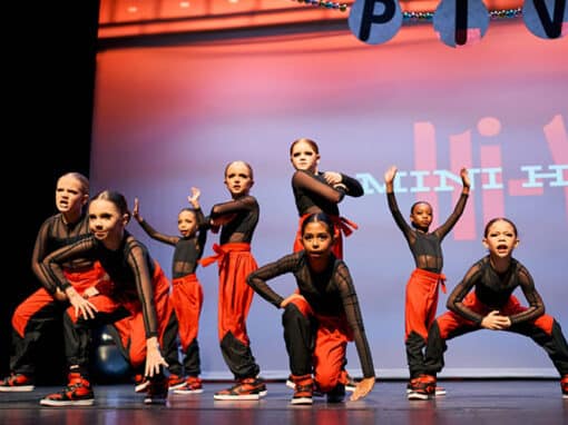 A group of young dancers in their black and orange costumes are performing on stage. A group of young dancers in their black and orange costumes are performing on stage.