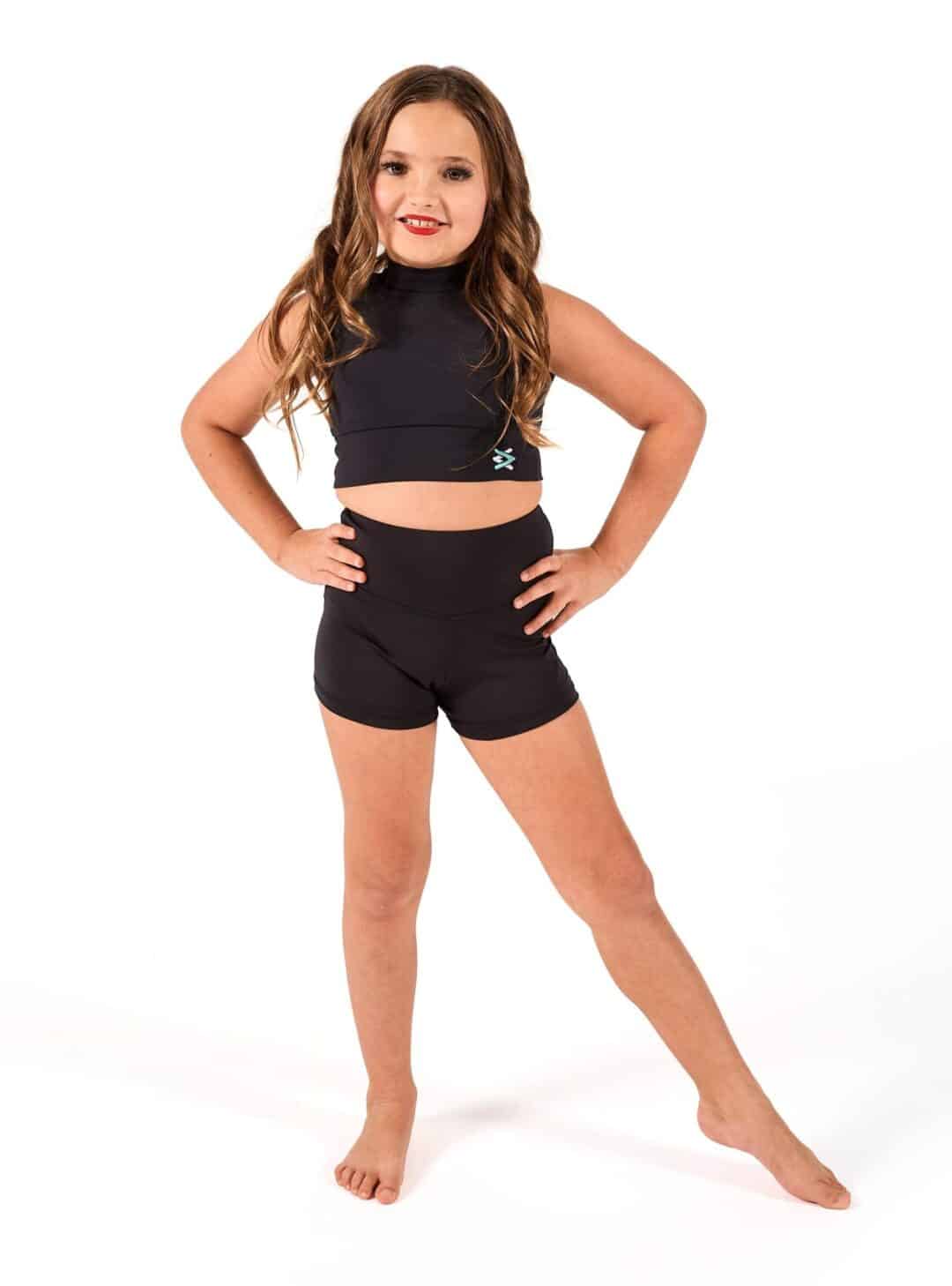 Young girl in black dance activewear standing confidently with hands on hips in a studio setting