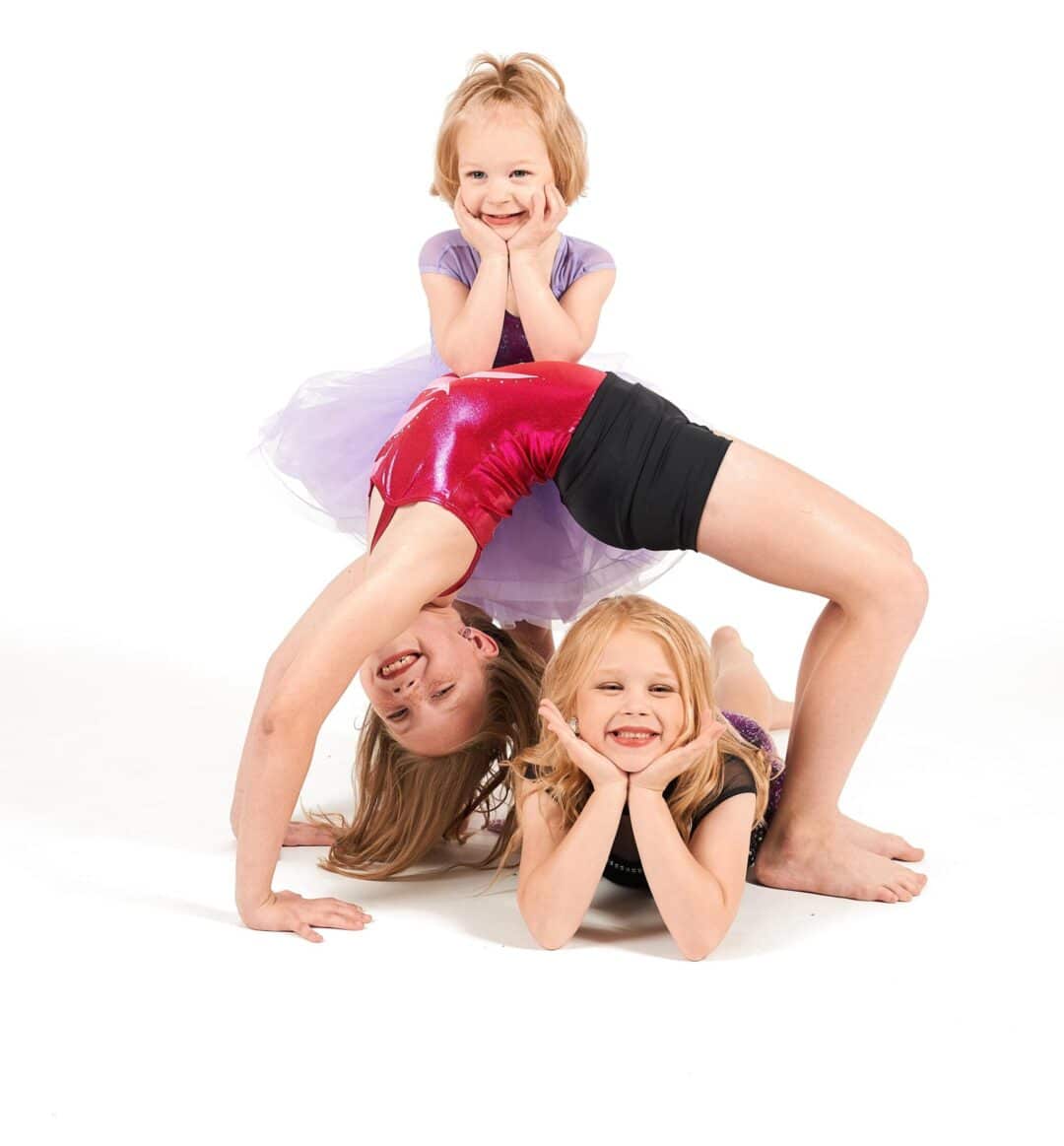 Three young girls in colorful dance outfits striking a playful group pose during a studio photoshoot