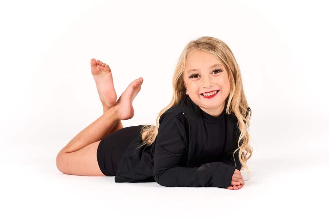 Young girl in black dancewear smiling and posing on the floor during a studio photoshoot