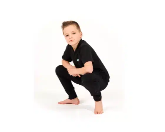Young boy in an all-black outfit crouches confidently on a white studio floor with a serious expression.