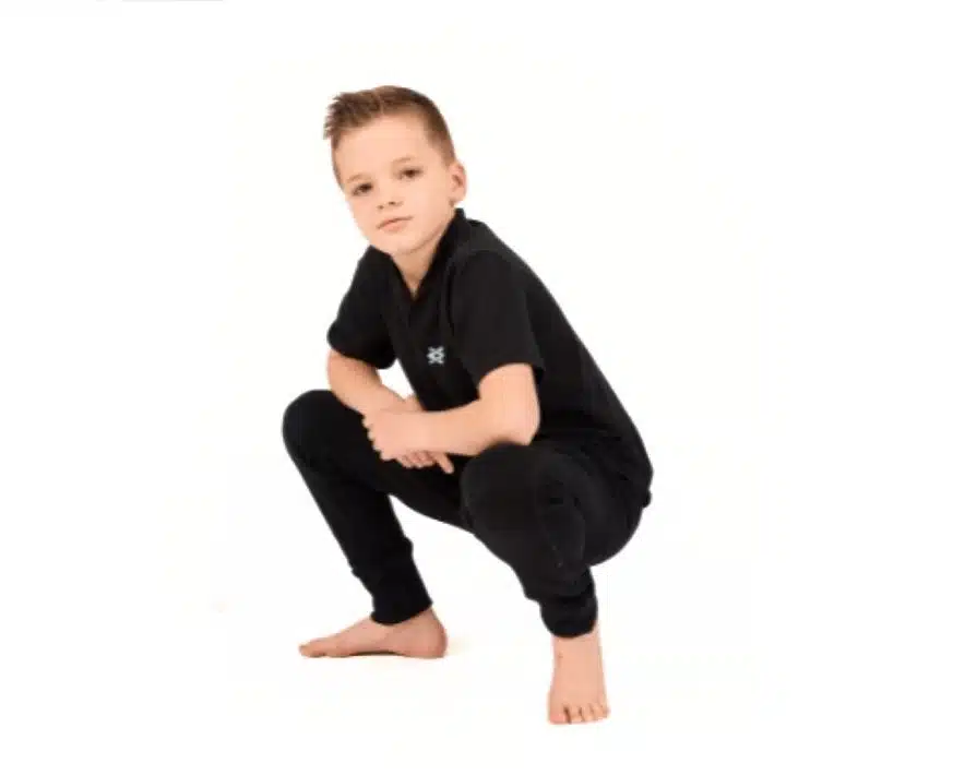 Pivot - Beginner Hip Hop Young boy in an all-black outfit crouches confidently on a white studio floor with a serious expression.